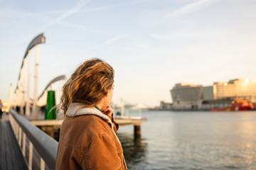 Blond girl with curly hair looking at the sunset by the sea in Barcelona, Catalonia, Spain.