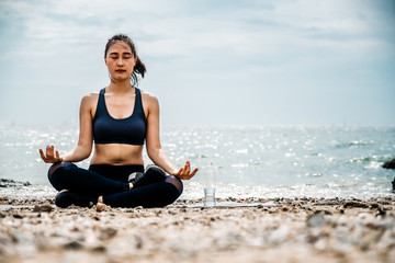 Young Asian woman practicing yoga exercise at quiet rock pier with sea background. Sport and recreation in city rush.