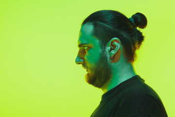 Portrait of a guy with colorful neon light on green studio background. Male model with calm and serious mood. Facial expression, cyberpunk, millenials lifestyle and look like. Future, technologies.