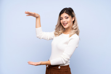 Young teenager girl over isolated blue background holding copyspace to insert an ad