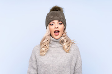 Young teenager girl with winter hat over isolated blue background with surprise facial expression