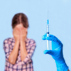 Hand in medical glove holds a syringe and the child is afraid of pricking with his eyes