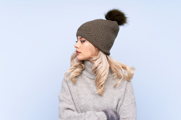 Young teenager girl with winter hat over isolated blue background looking side