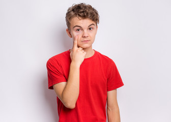Portrait of teen boy showing his eye. Child pointing with finger to eye. Caucasian young teenager, on gre background. Eyesight control. Medicine, people and health concept.