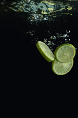 Fototapeta na wymiar Lime falls into the water. Fresh citrus in the water. Splash of water from falling into it slices of lime.