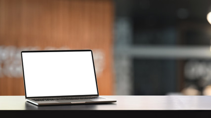 Photo of Computer laptop with white blank screen putting on modern wooden table with blurred living...