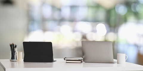Office desk workspace with laptop, tablet and office supplies on white table in modern office with blurred background. Concept of orderly workplace.