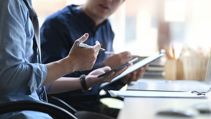 Cropped image of business developer team discussing/talking/meeting while sitting at the modern meeting table with orderly office as background.