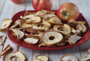 The benefits of dried fruits and vegetables. Dried apple chips and red fresh apples on a white wooden table on a red plate. Organic natural food.