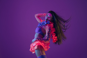 Motion, flying hairs. Hawaiian brunette model on purple studio background in neon light. Beautiful women in traditional clothes smiling and having fun. Bright holiday's, celebration colors, festival.