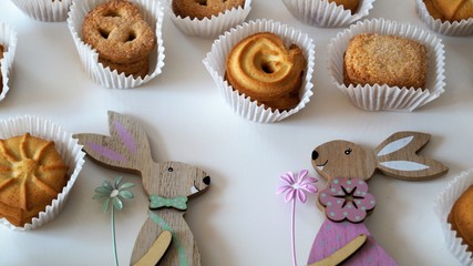 decorative wooden figures of hares with flowers and cookies in white pieces of paper on a white table