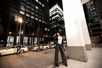 Stylish african american woman walking in night city. Woman dressed in trendy striped pants. Nightlife, evening city walks. Lifestyle concepts, fashion and style