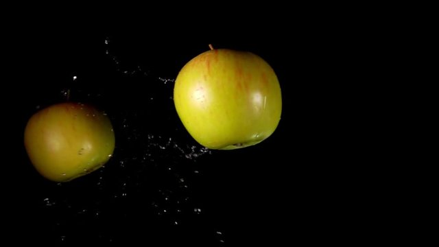 Two delicious green apples are flying and colliding with each other rising splashes of water in slow motion on the black background