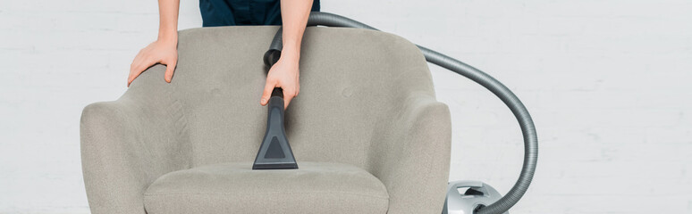 panoramic shot of young cleaner dry cleaning armchair with modern vacuum cleaner