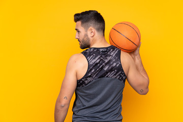 Obraz premium Man over isolated yellow background playing basketball in back position