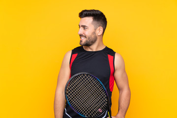 Tennis player man over isolated yellow wall looking side