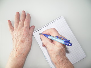 hands of an elderly man who writes in a notebook with a pen, on a white background