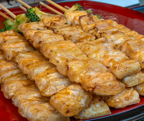 Salmon fillets and broccoli are skewered with sharp sticks to be grilled over fire, then painted with a seasoning sauce. When finished, it is ready for sale.