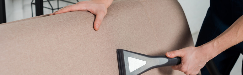 panoramic shot of man cleaning modern sofa with vacuum cleaner