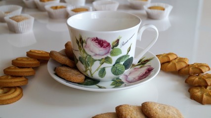 porcelain cup with a pattern in the form of a rose and cookies on a white table