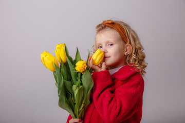 a child a blonde girl holding a bouquet of yellow tulips on a white background