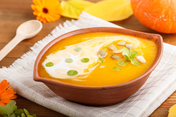 Traditional pumpkin cream soup with seeds in clay bowl on a brown wooden background with linen napkin. side view, selective focus.
