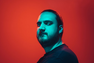 Portrait of a guy with colorful neon light on red studio background. Male model with calm and serious mood. Facial expression, cyberpunk, millenials lifestyle and look like. Future, technologies.