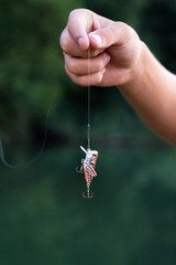 Male fisherman hand holding fishing bait on a string. Blurred green background