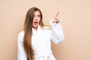 Fototapeta premium Teenager girl in a bathrobe over isolated background pointing away