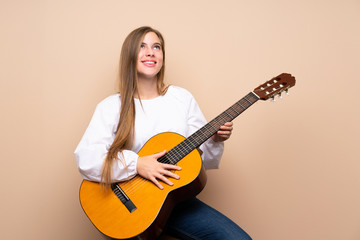 Teenager girl with guitar over isolated background looking up while smiling