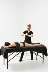 Funny fat burning massage. Portrait of cheerful woman masseur in uniforme near massage table with woman patient in wellness center. White background isolated