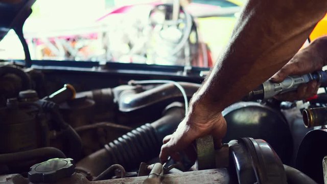 Mechanic man repairing car engine in garage.