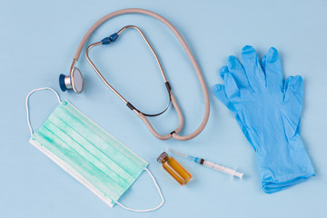 on a blue background a protective medical mask, syringe, medicine in a bottle, gloves and a stethoscope
