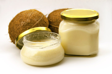 Solid homemade coconut oil in glass jar with metal gold lid and fresh coconuts on a white background
