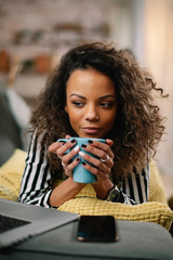 Young beautiful woman enjoying her coffee. African woman drinking coffee while using lap top.  