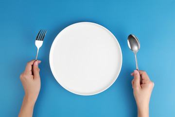 Female hands with cutlery and empty plate on coloured background. Meal preparation concept. Top view