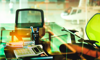 Office desk with documents,calculator,various office tools and blurry private helicopter parking in hangar airport indoor background.Business VIP Hospitality helicopter services for rented helicopter.