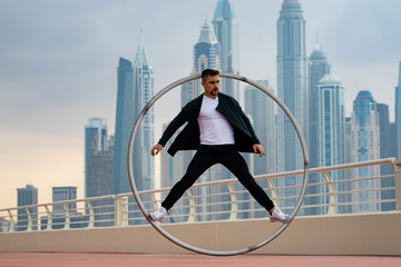 Cyr Wheel artist wearing black and white smart clothes with cityscape background of Dubai during sunset