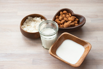 Homemade almond milk in a glass, almonds, milk and squeezed nut in bamboo bowl on wooden background