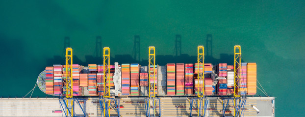 Aerial top view. Container ship in pier with crane bridge carries out export and import business in the open sea at daytime. Logistics and transportation. Banner background