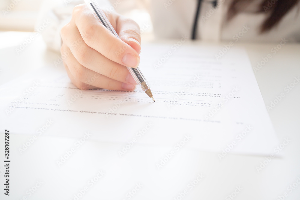 Wall mural Female hands hold a pen, write on a sheet of paper, fill out a form on a table