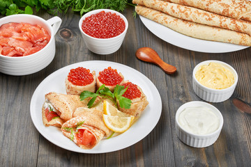 Delicious thin pancakes(blini) with fresh sour cream, red caviar and red fish on a white plate. Around a plates with fish, caviar, fresh butter and sour cream.  Holiday. Maslenitsa. Rustic style