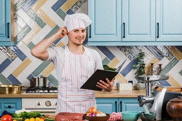 A male cook reads a recipe book near the table of fresh vegetables. Culinary art. Recipe for cooking healthy food