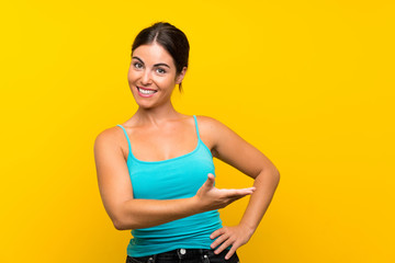Young woman over isolated yellow background extending hands to the side for inviting to come