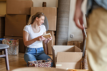 Young blond hair woman unpacking cardboard boxes at new home.Moving house