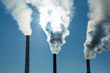 The smoking chimneys of a plant closeup. Pipes with thick smoke against a blue sky. Smoke-emitting...