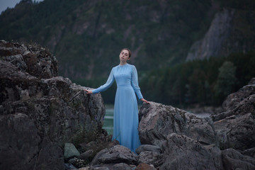 A girl in a blue dress stands on the banks of the river.