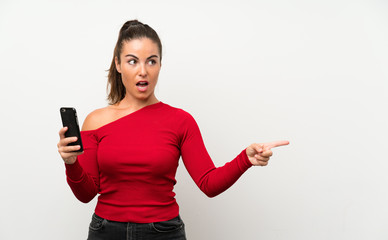 Young woman using mobile phone surprised and pointing finger to the side