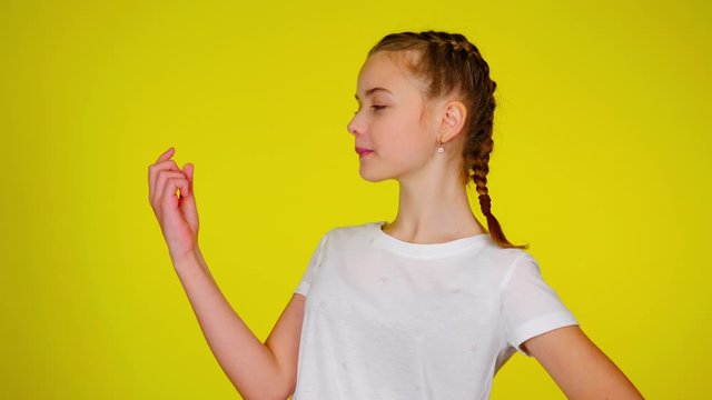 Teenage girl in a white T-shirt is looks at her manicure. Yellow background with copy space. Teenager emotions. 4k footage