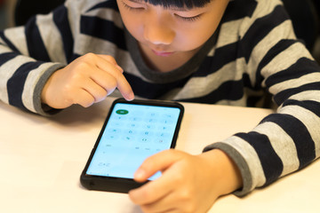 Young cute Asian boy use calculator app in smartphone to calculate simple and easy mathematic question (2+2) to check if his answer is correct. Early mathematic education and digital literary concept